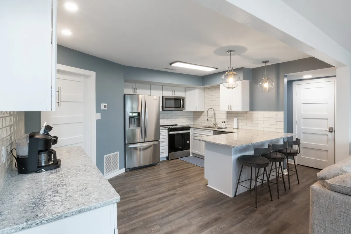 A stylish kitchen with a prominent island, stainless steel appliances, pendant lighting, and granite countertops. The setting invites group meal prep and casual conversations, emphasizing the fully stocked and modern appeal of the home’s kitchen area.