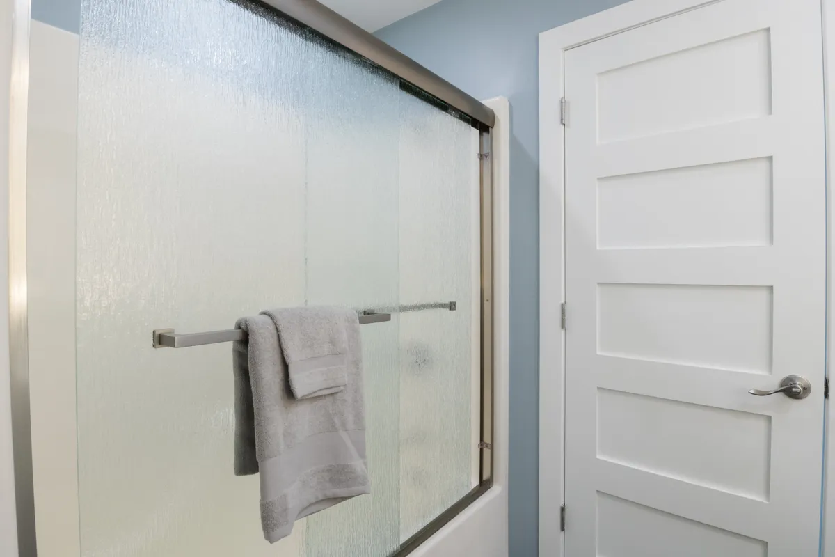 A contemporary bathroom highlighted by a glass shower door, a soft white towel on the rack, and a clean, uncluttered aesthetic. The space is bright and calming, ideal for self-care and relaxation after a day of lakeside fun.