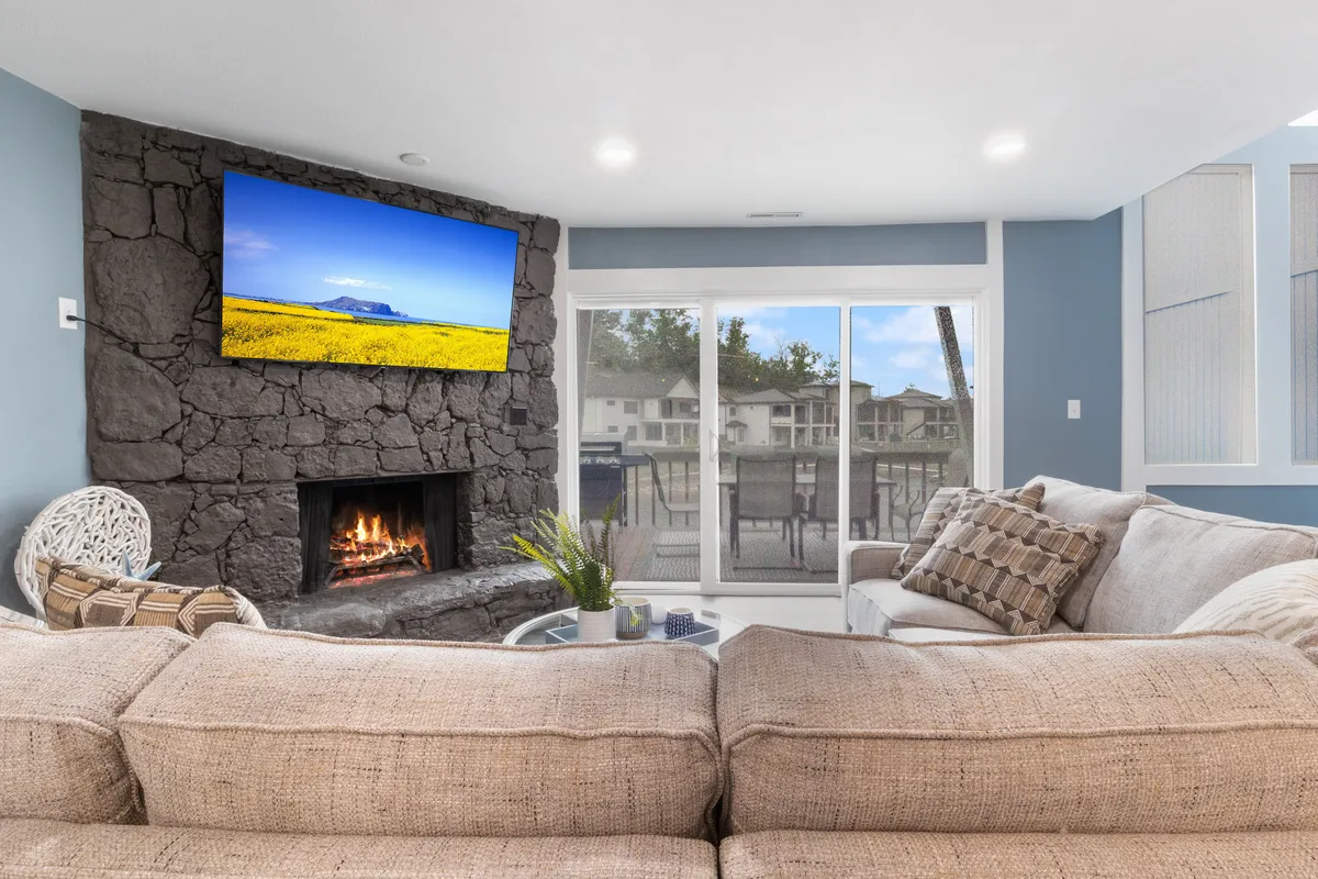 A cozy living area featuring a fireplace, a comfortable sofa positioned toward a large TV, and sliding glass doors that reveal a glimpse of the outdoors and lake views beyond. Soft lighting and inviting textures create a romantic ambiance, and the view outside hints at sunsets and lakeside relaxation.