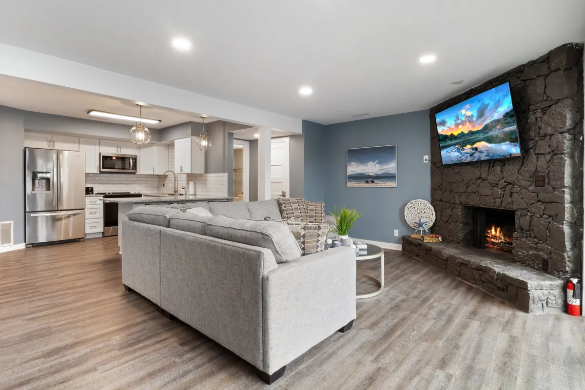 A cozy, inviting living area with a plush sofa, fireplace, large TV, and a kitchen area in the background. The space feels perfect for gathering, relaxing, entertaining, or unwinding after a day of adventure.