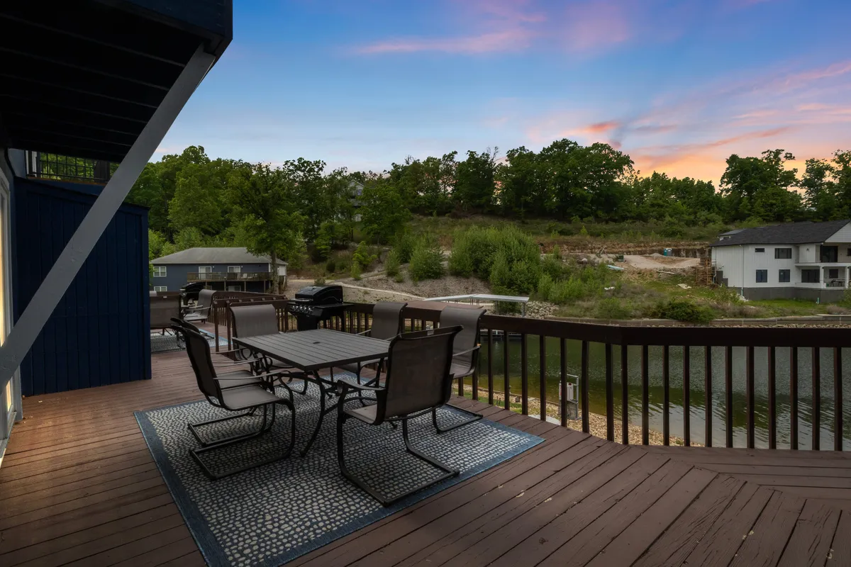 An inviting outdoor dining setup on the dock or dockside patio, with a table and chairs overlooking the water and surrounded by greenery. The scene suggests opportunities for alfresco dining, morning coffee, or gathering with friends and family as the sun sets over the lake.