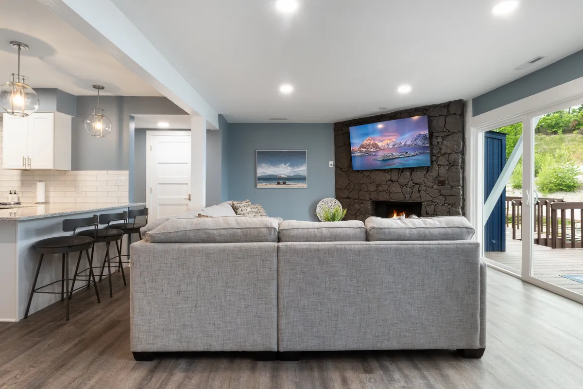 This scene captures a comfortable sofa with a television and a stone fireplace, adjacent to a kitchen bar area with seating. The space is accented by modern artwork and offers a relaxed, welcoming atmosphere ideal for unwinding with friends after exploring local nightlife.